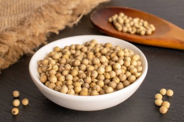 Fragrant vegetable coriander seeds in white plate with wooden spoon and jute napkin on slate stone, macro.