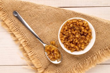 Yellow gelatin granules in white plate with metal spoon and jute napkin on wooden table, macro, top view.