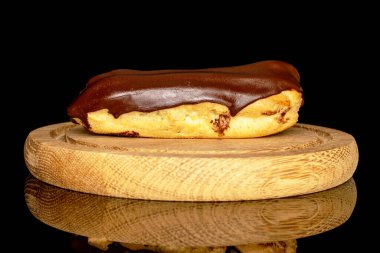 One chocolate eclair on a wooden tray, macro, isolated on black background.