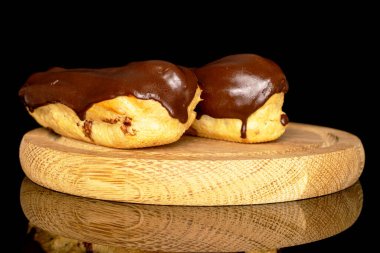 Two chocolate eclairs on a wooden tray, macro, isolated on black background.