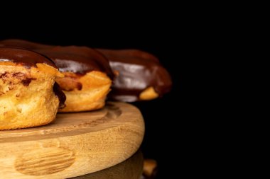Three chocolate eclairs on a wooden tray, macro, isolated on black background.