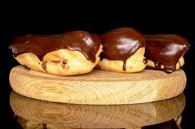 Three chocolate eclairs on a wooden tray, macro, isolated on black background.