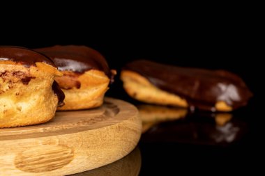 Three chocolate eclairs on a wooden tray, macro, isolated on black background.