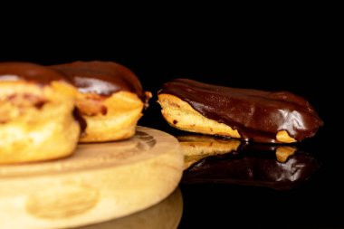 Three chocolate eclairs on a wooden tray, macro, isolated on black background.