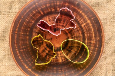  Three cookie cutters with a clay plate on a jute cloth, macro, top view.