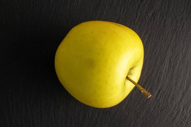One yellow organic apple on slate stone, macro, top view.