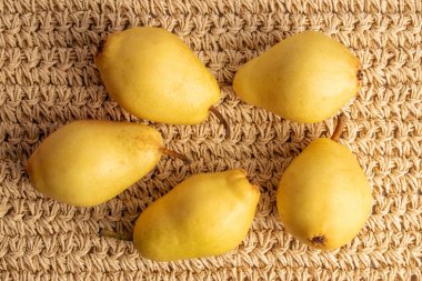 Several organic yellow pears, close-up, on a straw mat, top view.