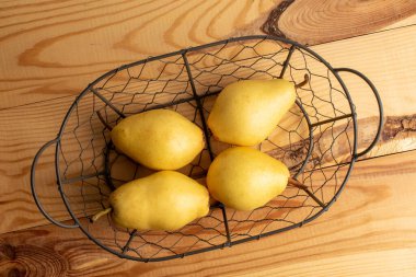 Four ripe yellow pears in a wicker basket, close-up, on a white wooden table, top view.