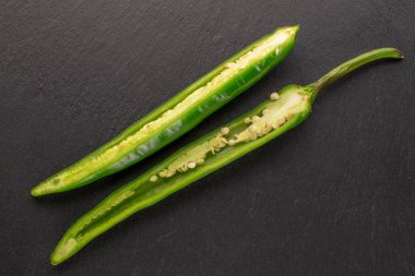 Two halves of green hot peppers on a slate stone, macro, top view.
