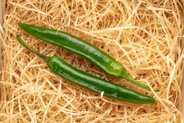 Two green spicy peppers on straw, macro, view from above.