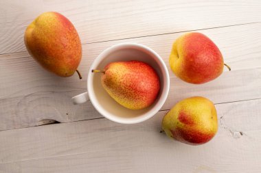 Dört olgun sarı-kırmızı armut, beyaz ahşap bir masanın üstünde, üst tarafta..