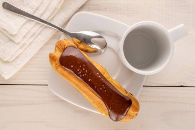 Beyaz seramik tabağı olan bir çikolatalı pasta, tahta masa üzerinde fincan ve metal kaşık, yakın plan, üst görüş..