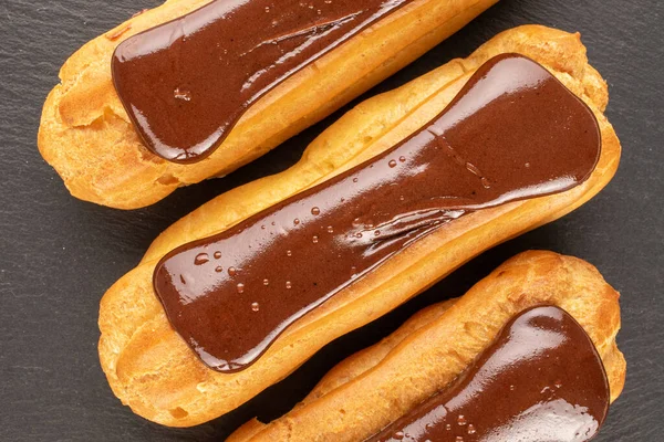 stock image Three chocolate eclairs, close-up, on slate stone, top view.