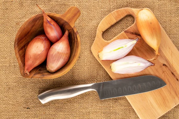 stock image A few organic onions with a wooden cup and two halves with wooden board and knife on jute canvas, macro, top view.