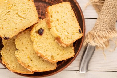 Dilimlenmiş ev yapımı kuru üzümlü kek, kil tabağı ve metal bıçakla ahşap masa, makro, üst manzara..
