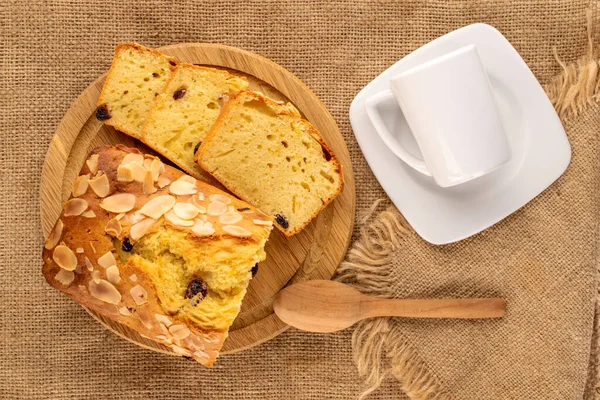 Dilimlenmiş ev yapımı kuru üzümlü kek, ahşap tepsiyle ve fincanlı beyaz fincan tabağı jute kumaş, makro, üst manzara..