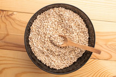 Siyah bir kâse içinde organik inci arpası, ahşap bir masa üzerinde ahşap bir kaşık, yakın plan, üst manzara..