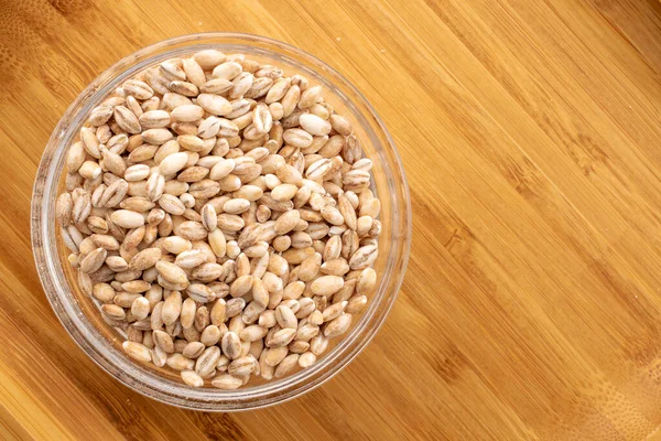 stock image Organic pearl barley in a glass plate on a wooden table, close-up, top view.