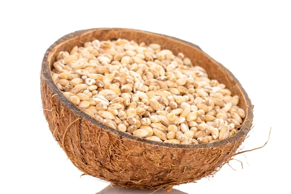Organic pearl barley in a coconut shell, close-up, isolated on white.
