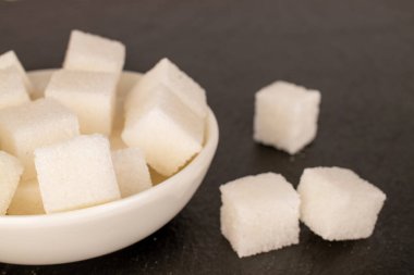 Birkaç küp beyaz şeker ve beyaz bir tabağı kayrak taşı üzerinde, makro..