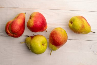 Beyaz ahşap bir masa üzerinde birkaç olgun organik armut..
