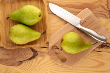 Üç organik armut, ahşap mutfak tahtası, bambu tabağı ve metal bıçak ahşap masa, makro, üst görünüm.