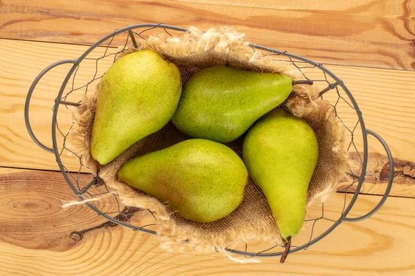 Four organic pears with jute napkin in basket on wooden table, macro, top view.