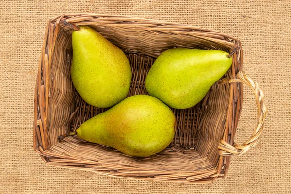 Three organic pears in a basket on a jute cloth, macro, top view.