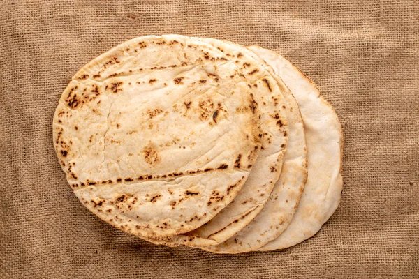 stock image Four freshly baked pita bread on burlap, close-up, top view.