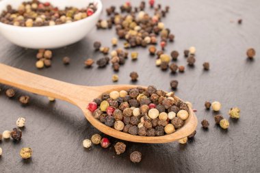 Tahta bir kaşıkla, makroyla beyaz bir tabak üzerinde dört biber tanesinin karışımı..