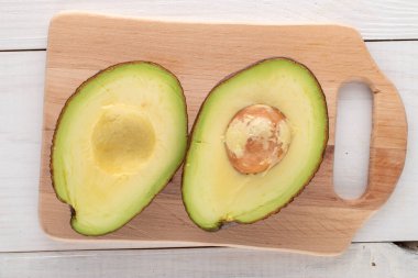 Ahşap bir masanın üzerinde iki yarım organik olgun avokado, yakın plan, üst manzara..