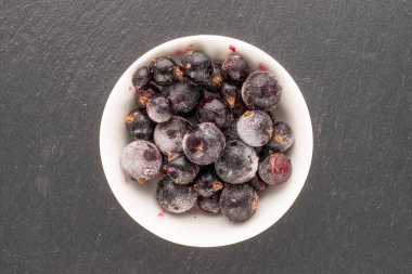 Donmuş siyah frenk üzümü, beyaz çay tabağı, kayrak taşı, makro, üst manzara..