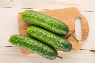 Tahta bir masa üzerinde ahşap mutfak tahtasıyla üç olgun yeşil salatalık..