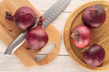 Tahta tepside organik mavi soğanlar, ahşap masada bıçak ve mutfak tahtası, makro, üst manzara..