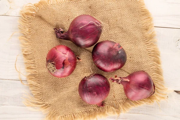 Several organic blue onions with jute napkin on wooden table, macro, top view.