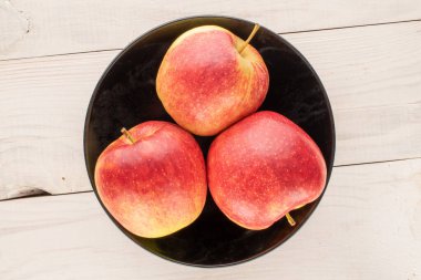 Tahta bir masada siyah seramik bir tabakta üç organik kırmızı elma, makro, üst manzara..