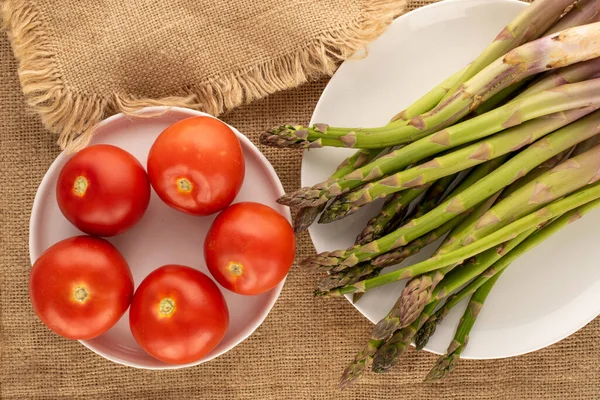 Several Stalks Organic Asparagus Five Tomatoes White Ceramic Plates Jute — Stock Photo, Image