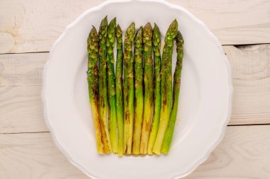 Ahşap bir masada seramik beyaz bir tabakta ızgara kuşkonmaz, makro, üst manzara..