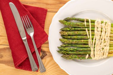 Seramik beyaz bir tabakta, ahşap bir masada, çatal ve bıçakla ızgara kuşkonmaz, makro, üst manzara..