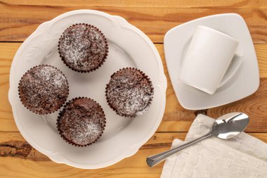 Tahta bir masanın üzerinde beyaz seramik tabakları olan dört ev yapımı çikolatalı kek, makro, üst manzara..