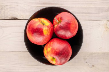 Tahta bir masada siyah bir seramik tabakta üç kırmızı elma, makro, üst manzara..