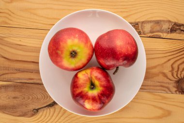 Tahta bir masada beyaz bir seramik tabakta üç kırmızı elma, makro, üst manzara..