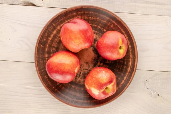 stock image Four ripe nectarines with a white plate on a wooden table, macro, top view.