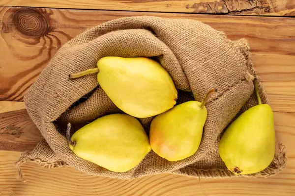 stock image Several bright yellow pears with a jute bag on a wooden table, macro, top view.