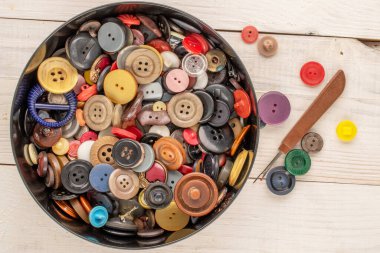 Tahta bir masa, makro, üst görünüm üzerinde plastik bir kapta bir sürü düğme.