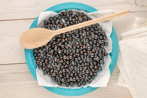 Stock image Several organic blackcurrant berries with plate, wooden spoon and linen napkin on wooden table, macro, top view.