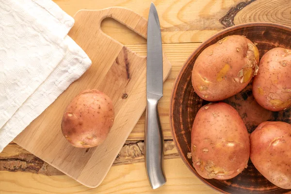 几种生粉土豆 有粘土盘 厨房木板和金属刀 宏观的 放在木制桌子上 顶部视图 — 图库照片