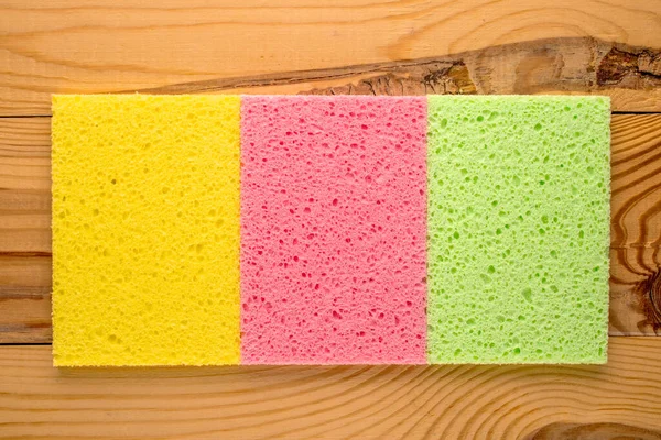 stock image Three colored cellulose kitchen sponges on a wooden table, macro, top view.