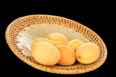 Seramik tabakta birkaç organik sarı kayısı, makro, siyah arka planda izole edilmiş..