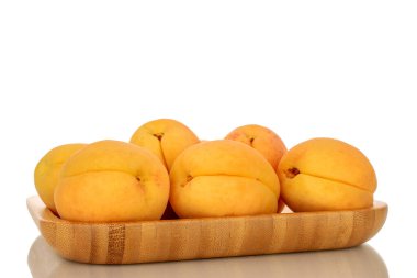 Bambu tepsisinde birkaç parlak sarı kayısı, makro, beyaz bir arka planda izole edilmiş..